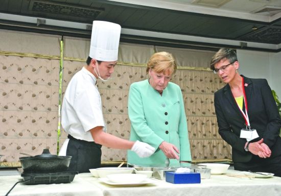 6日，德国总理默克尔（中）正在学习川菜宫保鸡丁的做法 新华社发
